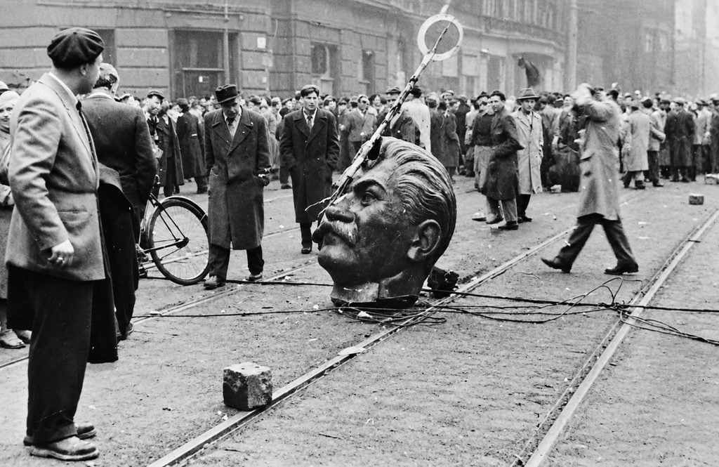 Ľudia v Budapešti stoja okolo zvrhnutej hlavy Stalinovej sochy počas povstania v roku 1956